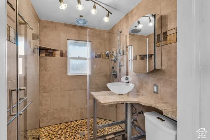 Walk-in shower with glass enclosure, stone-finish wall tile, vessel sink on a stone-topped vanity, and multidirectional track lighting