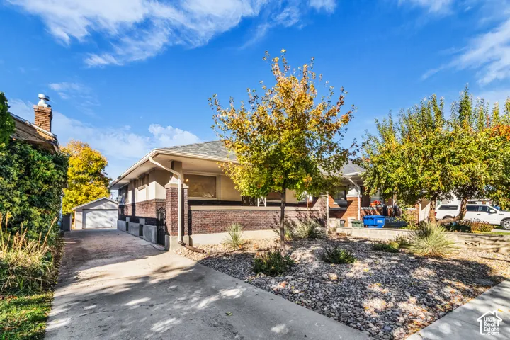 Single-story residence featuring brick exterior masonry, a covered porch, concrete driveway, and a detached garage