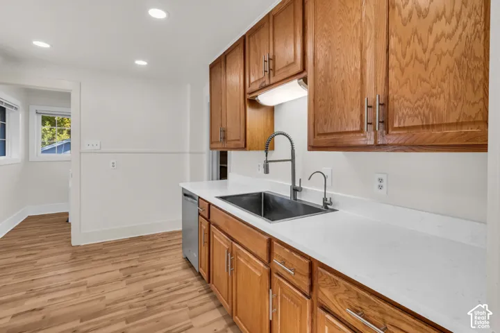 Kitchen featuring wood cabinetry, white stone-finish countertops, stainless steel undermount sink with a gooseneck faucet, recessed lighting, and wood-finish flooring