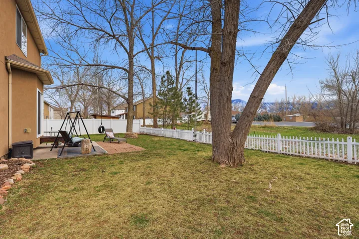 Backyard featuring a paved brick patio, white vinyl fencing, mature trees, and mountain scenery