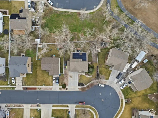 Aerial view of residential property featuring a solar panel array, concrete driveway, fenced yard, and mature trees