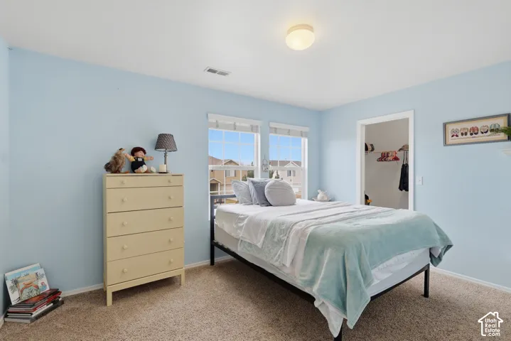 Room featuring neutral-toned carpeting, dual grid-pattern windows, and a walk-in closet