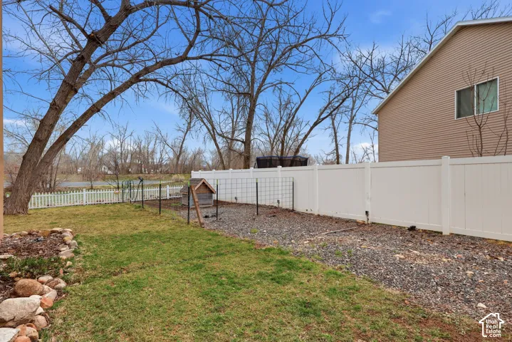 Backyard featuring a privacy-style vinyl fence, stone-ground landscaping, natural grass areas, and decorative rock border