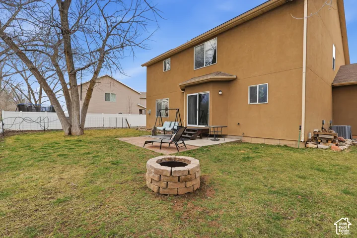 Stucco exterior residence featuring a paved rear patio, circular masonry fire pit, and white perimeter fencing