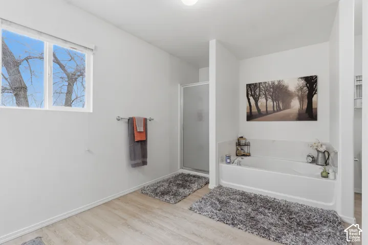 Bathroom featuring wood-finish flooring, a soaking tub with a tiled surround, a separate enclosed shower, and a window providing natural light