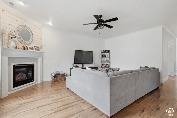 Living area featuring wood-finish flooring, a fireplace with a white mantel, horizontal wood-plank wall detailing, and a ceiling fan with integrated lighting