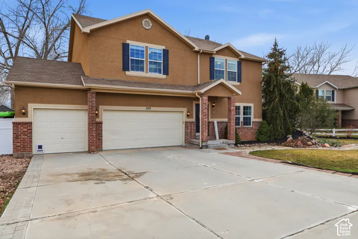 Two-story exterior featuring a stucco facade, red brick accents, three-car garage, and dark-toned shutters