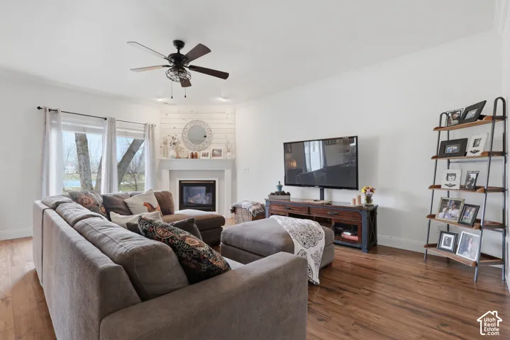 Living area featuring wood-finish flooring, a corner fireplace with horizontal shiplap detailing, crown molding, and a central ceiling fan
