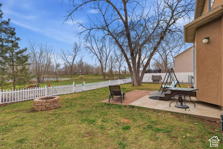 Private backyard featuring a paved stone patio, a circular masonry fire pit, mature trees, and white vinyl privacy fencing