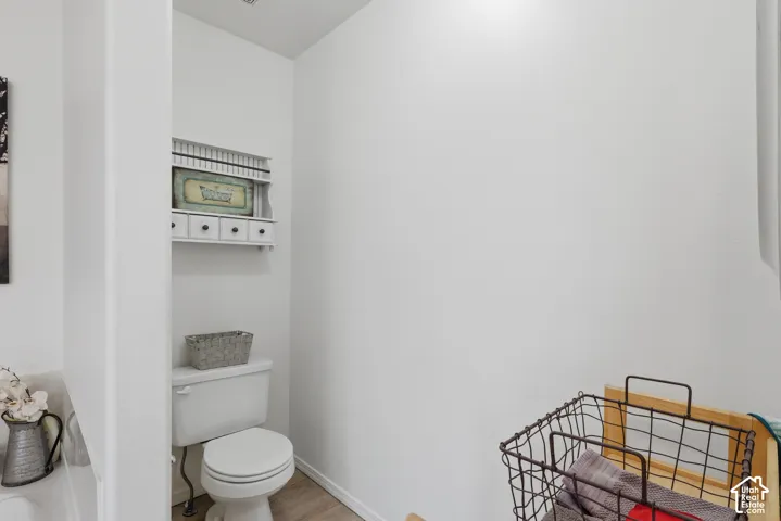 Standard-height toilet with a white finish, wood-finish flooring, and white wall-mounted storage unit