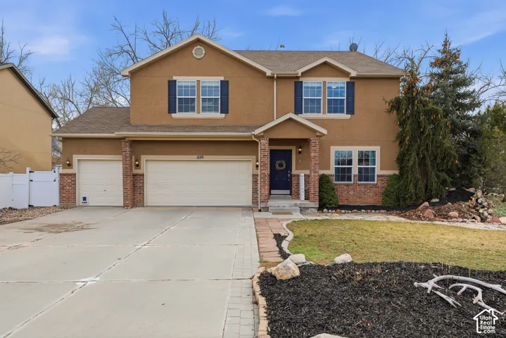 Two-story stucco exterior featuring brick accents, a covered front entryway, multi-pane windows with decorative shutters, and an attached three-car garage