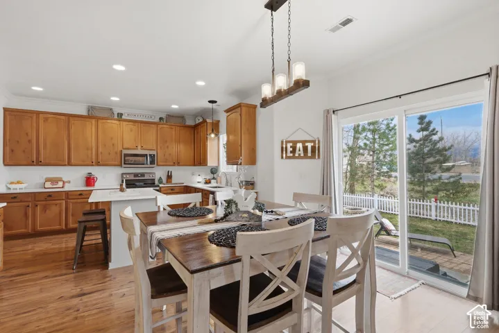 Open-concept kitchen and dining area featuring wood-finish cabinetry, an island with stone-surface countertop, recessed lighting, and a linear multi-light pendant fixture