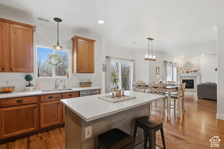 Kitchen featuring warm-tone cabinetry, central island with a solid surface countertop, white tile backsplash, wood-finish flooring, and pendant lighting