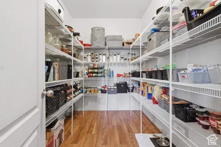 Walk-in pantry featuring white wire shelving units and wood-finish flooring