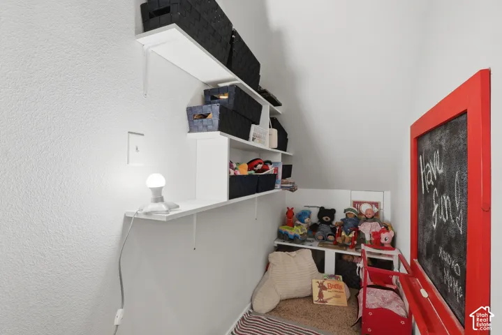 Under the stairs play area on main level. Built-in wall-mounted white shelving units and a wall-mounted chalkboard framed in red