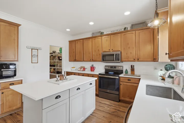 Kitchen featuring medium-toned wood cabinetry, quartz countertops, a central island with painted cabinetry, stainless steel appliances, and white subway tile backsplash