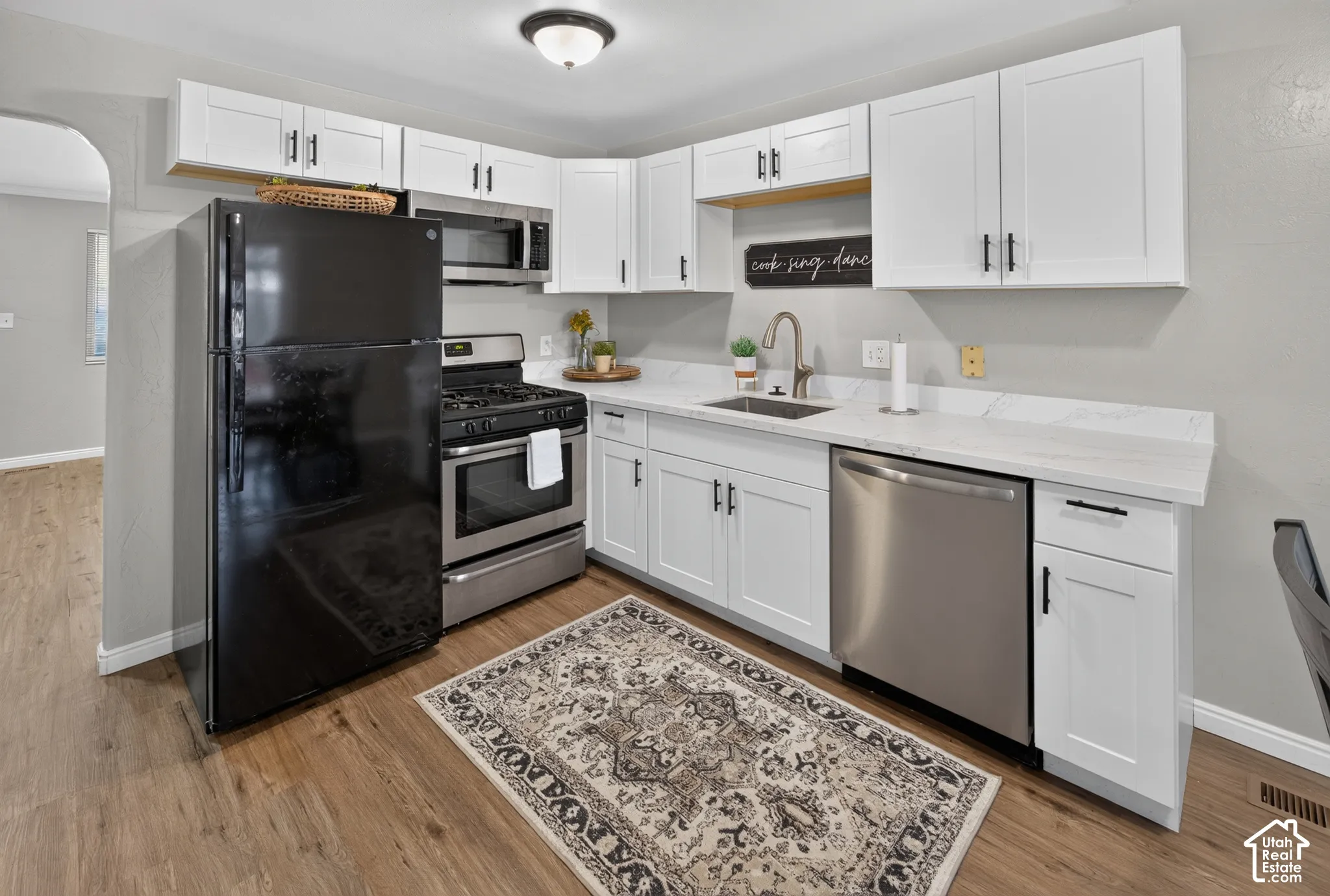 Kitchen featuring white shaker-style cabinetry, white countertops with grey veining, stainless steel appliances, and wood-finish flooring
