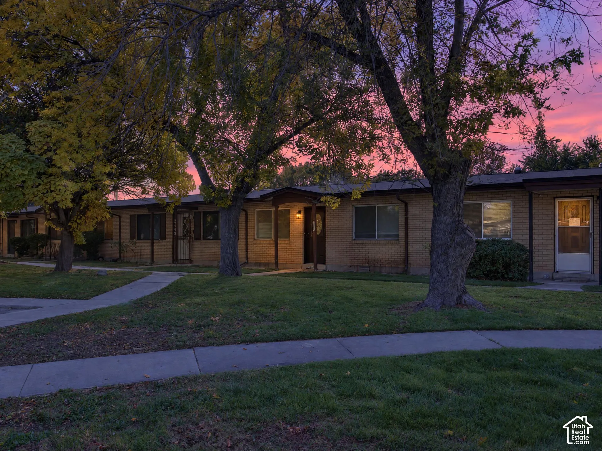 Single-story brick exterior featuring concrete walkways, mature shade trees, and a low-sloped roofline