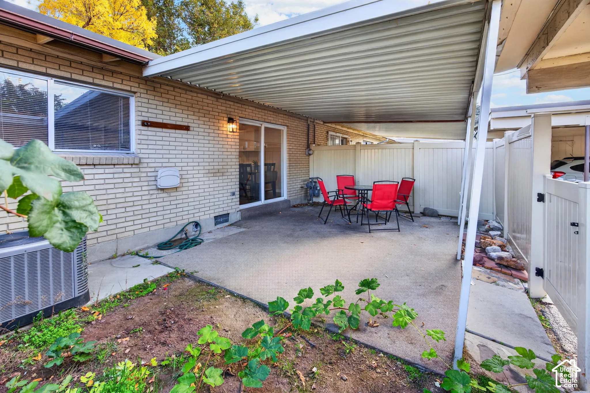 Brick exterior featuring a concrete patio, a metal-roofed covered area, and a white privacy fence