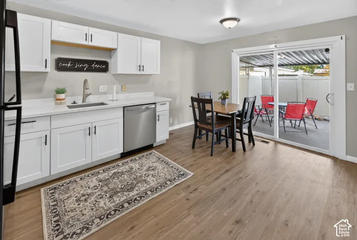 Kitchen featuring white shaker-style cabinetry, solid-surface countertops, a stainless steel dishwasher, wood-finish flooring, and a sliding glass door