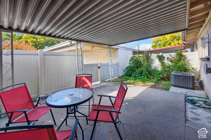 Covered patio featuring a corrugated metal roof, concrete flooring, decorative metal supports, and enclosed by white vinyl privacy fencing