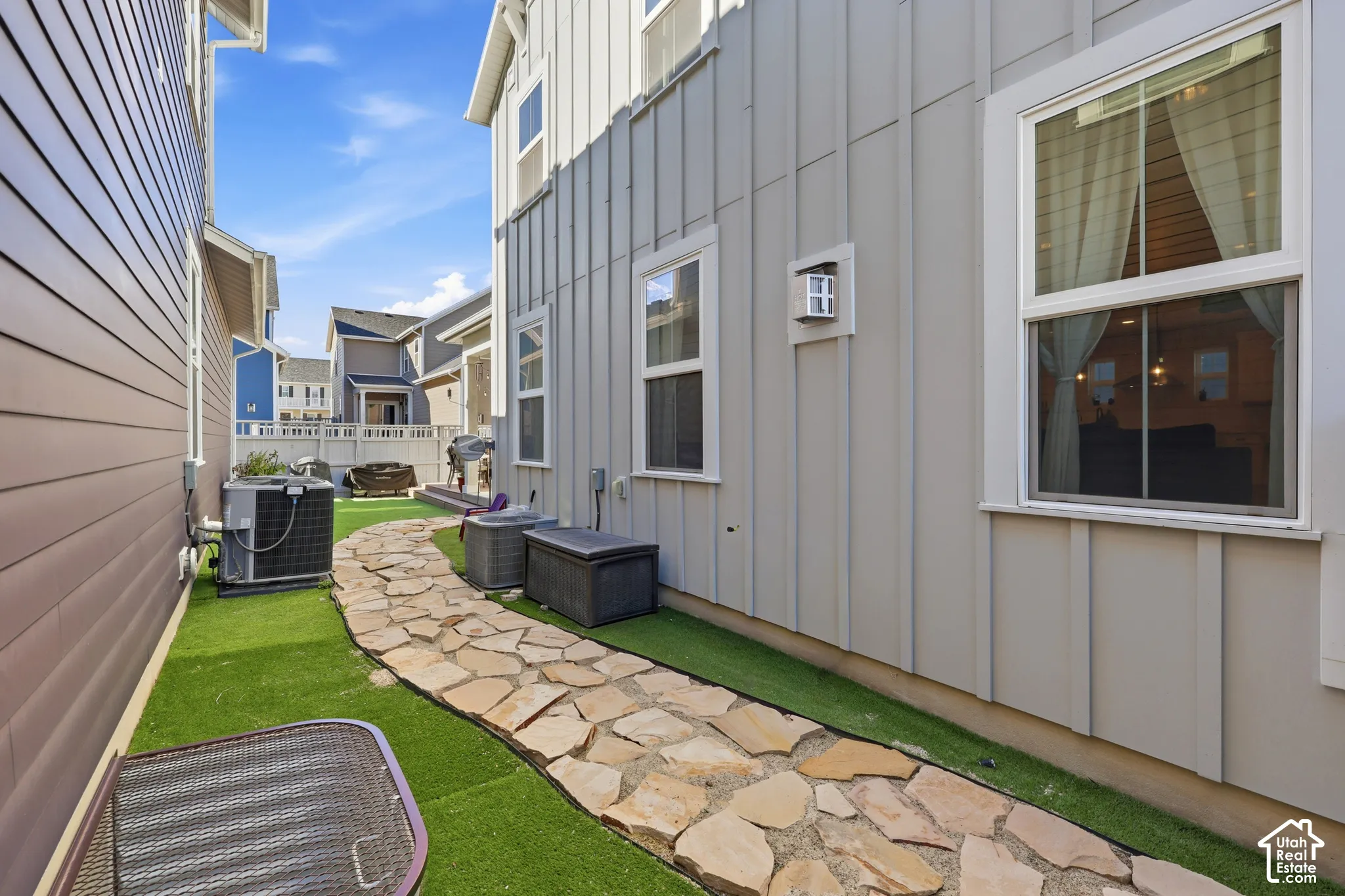 Vertical board-and-batten siding, stone-paver walkway, and low-maintenance synthetic turf landscaping