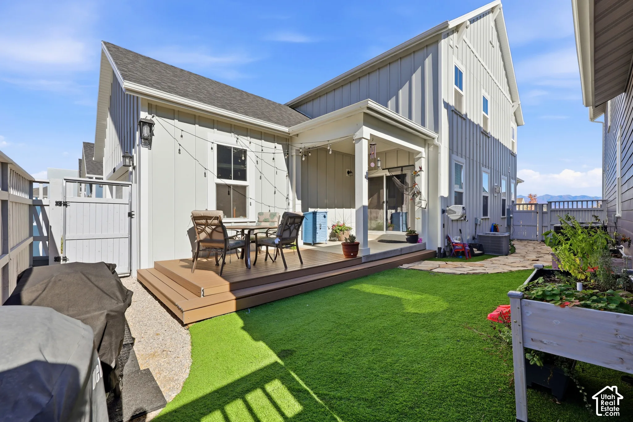 Rear exterior featuring board-and-batten siding, a covered patio, a synthetic lawn, a multi-level composite deck, and stone paver pathways