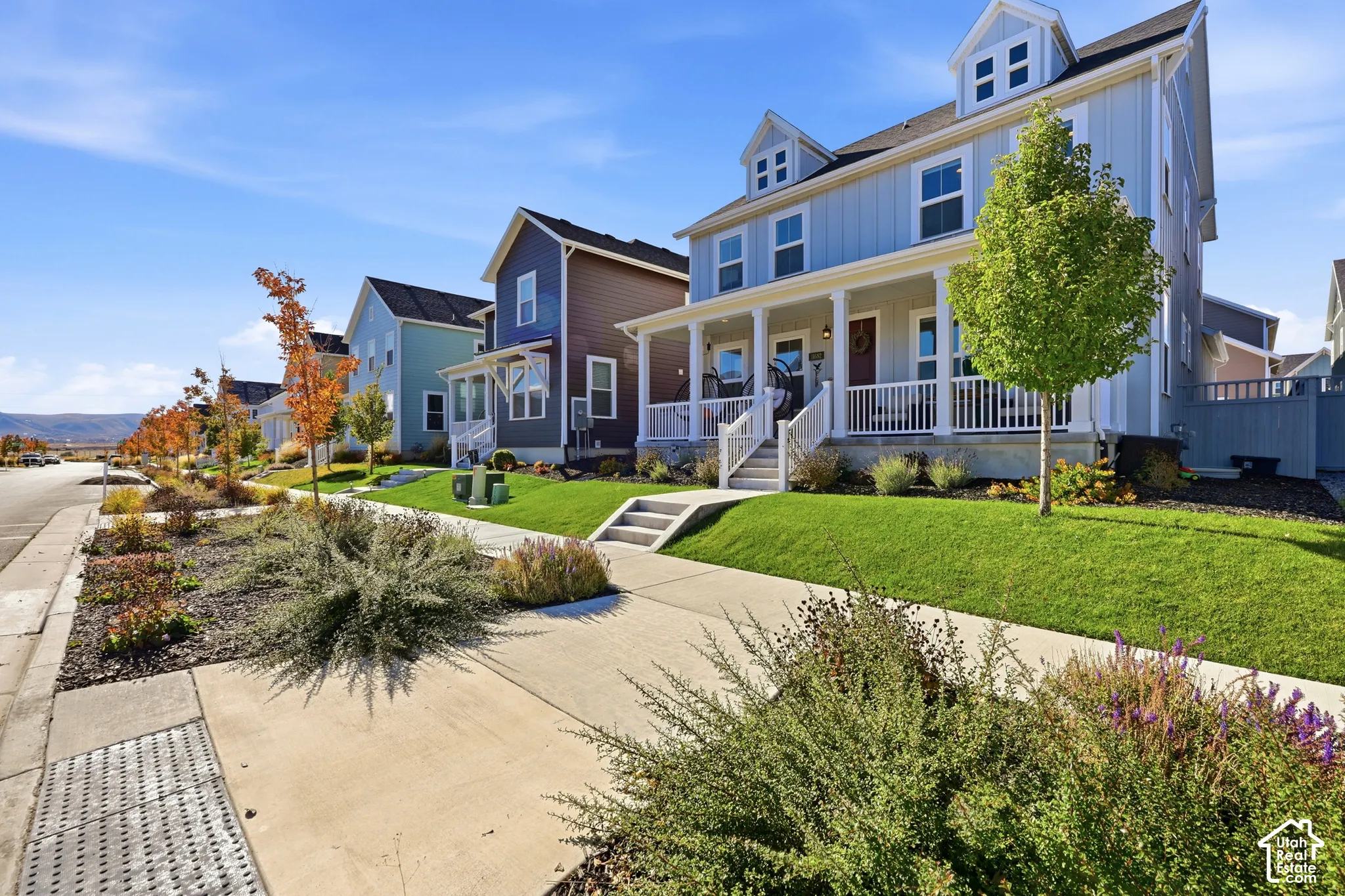 Two-story home with vertical siding, a covered front porch, white railings, dormer windows, and a manicured lawn