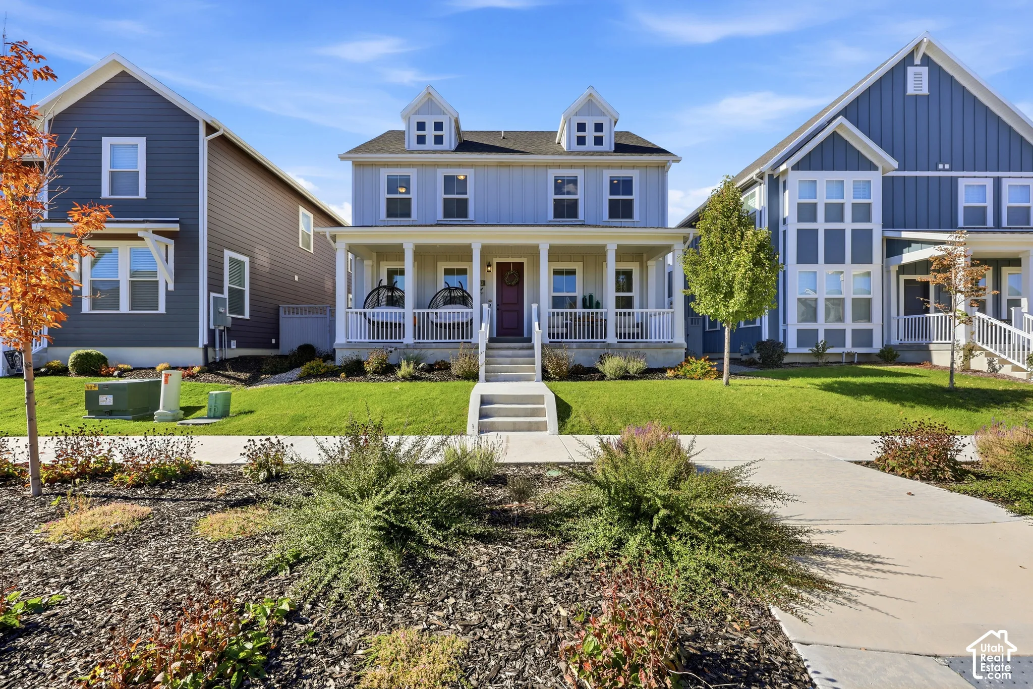 Two-story residence featuring vertical board-and-batten siding, a covered front porch with white railing, double dormer windows, and a concrete front walkway