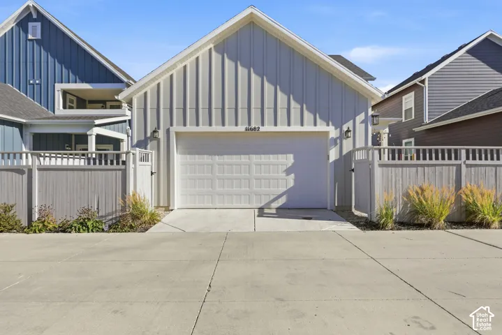 Vertical board-and-batten siding, concrete driveway, attached garage, and perimeter privacy fencing