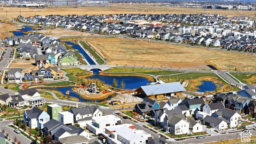 Aerial perspective of a master-planned community featuring multi-level residential architecture, central water features, pedestrian pathways, and a large-scale community building with a metal roof