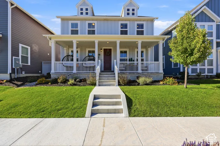 Two-story residence featuring a covered front porch with white railing, vertical board siding, dual roof dormers, and a concrete walkway with integrated steps
