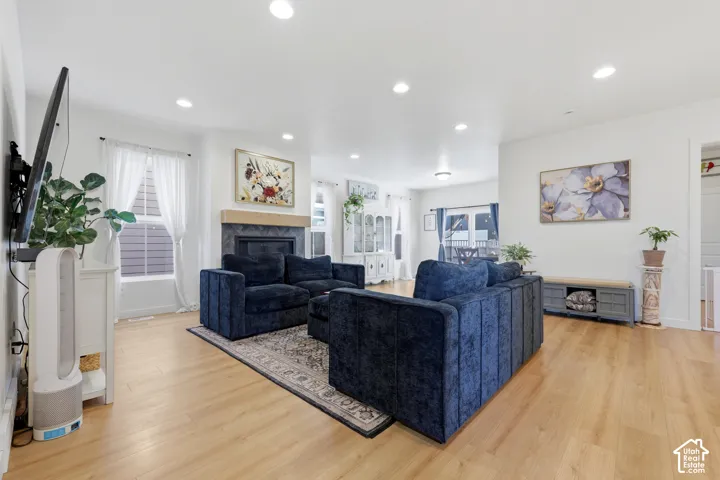 Open-concept living area featuring wood-finish flooring, recessed lighting, and a fireplace with a decorative tile surround and natural wood mantel