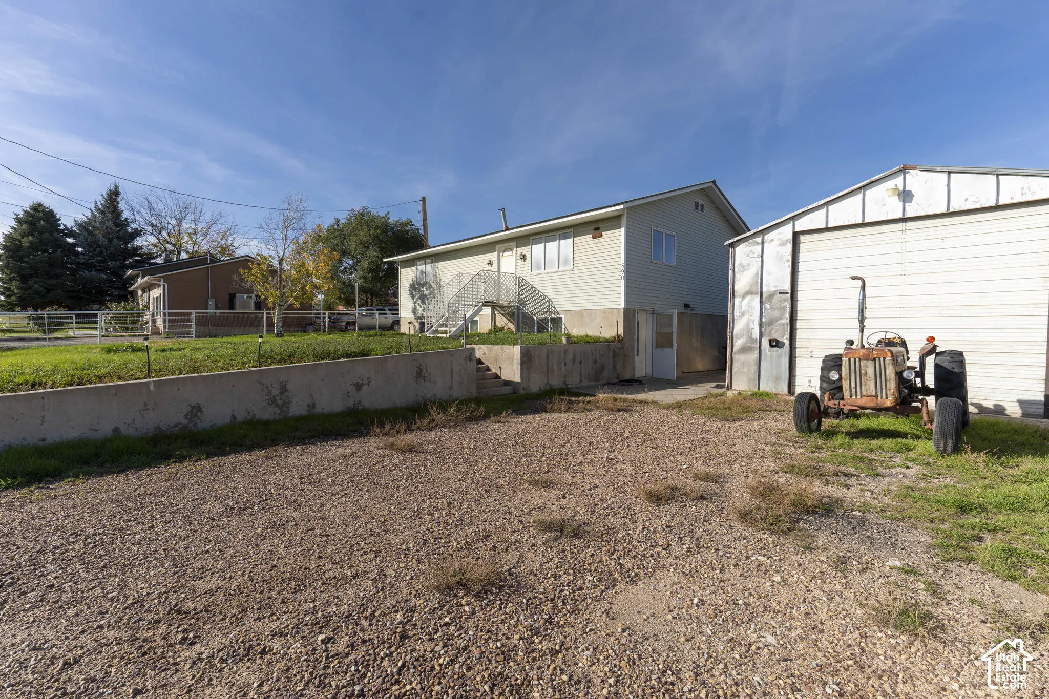 Exterior view featuring vinyl siding, a raised main entry with metal staircase, a concrete retaining wall, and a detached metal-sided storage structure