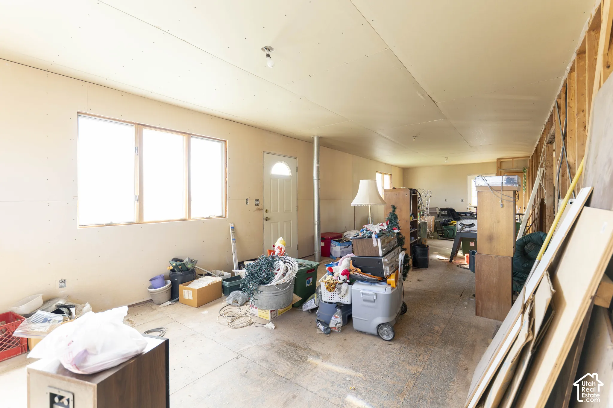 Open-concept interior featuring exposed wood-stud framing, unfinished drywall wall panels, multi-pane windows, and a singular exterior entry door