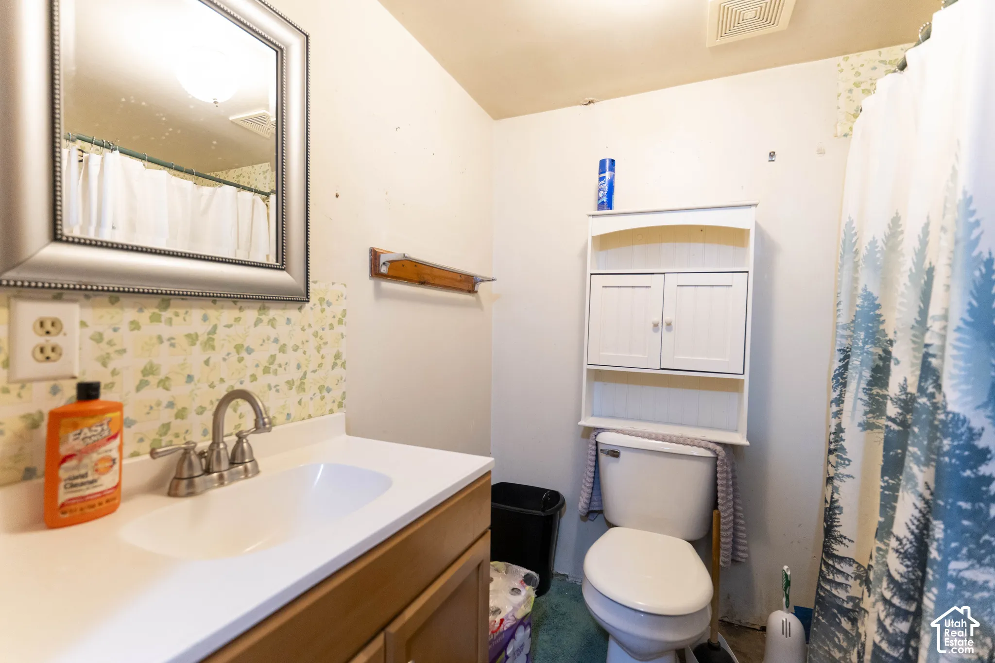 Bathroom featuring a vanity with a white countertop, integrated basin, dual-handle faucet, wall-mounted mirror, and built-in white cabinetry above the toilet