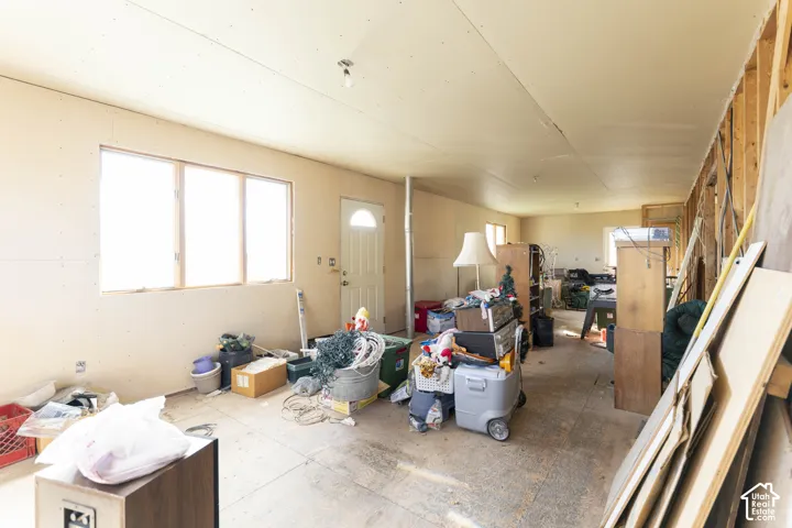Open-concept interior featuring exposed wood-stud framing, unfinished drywall wall panels, multi-pane windows, and a singular exterior entry door
