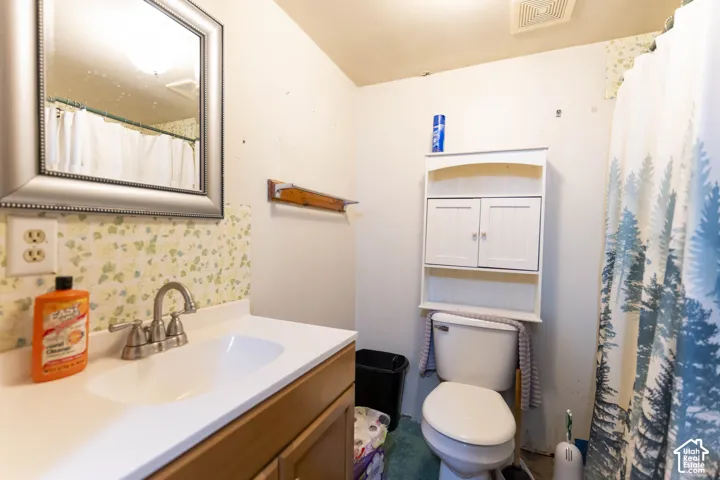 Bathroom featuring a vanity with a white countertop, integrated basin, dual-handle faucet, wall-mounted mirror, and built-in white cabinetry above the toilet