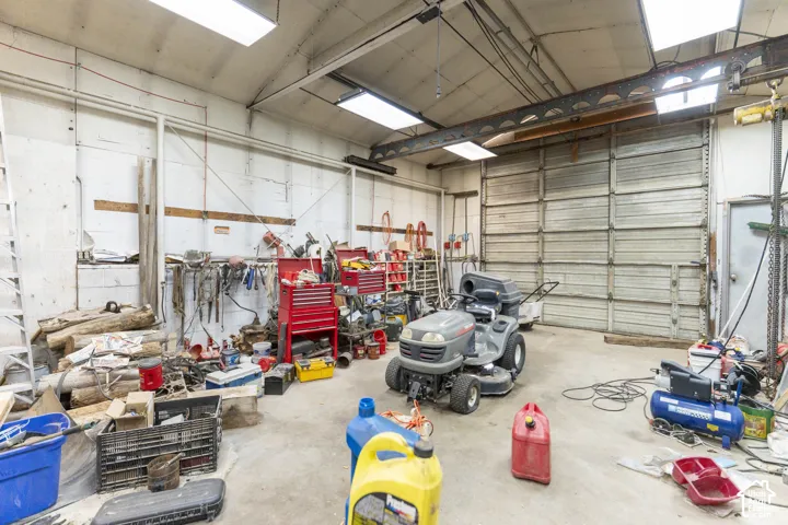Industrial workshop space featuring concrete flooring, high ceilings with exposed steel beams, an overhead crane system, and a large metal roll-up garage door