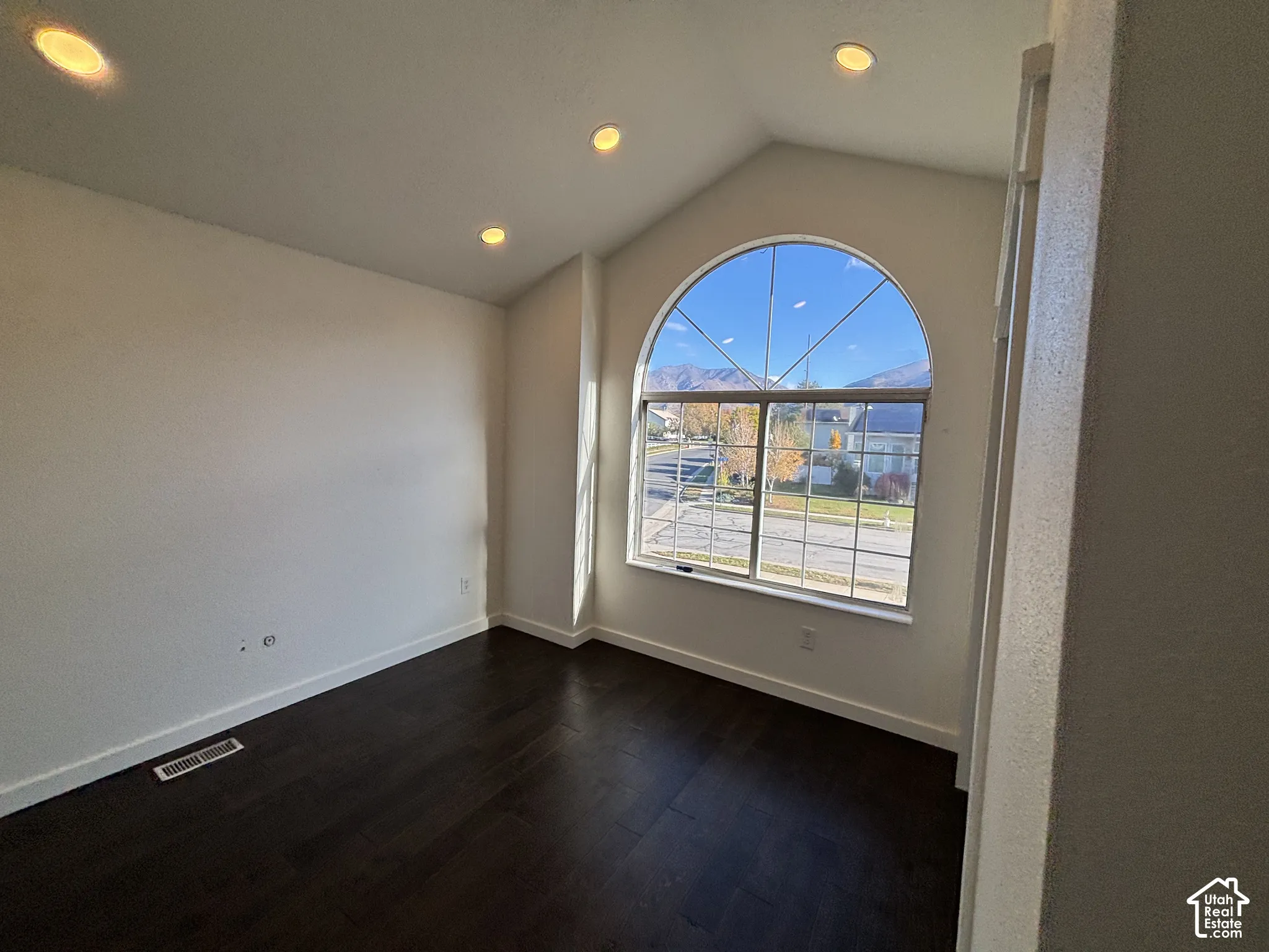 Vaulted ceiling with recessed lighting, wood-finish flooring, and a large arched window with mountain backdrop