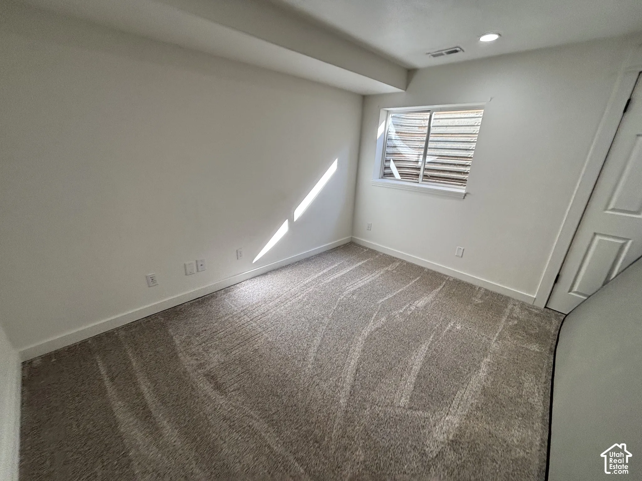 Neutral-toned carpet, recessed lighting, and a slider-style window with a window well