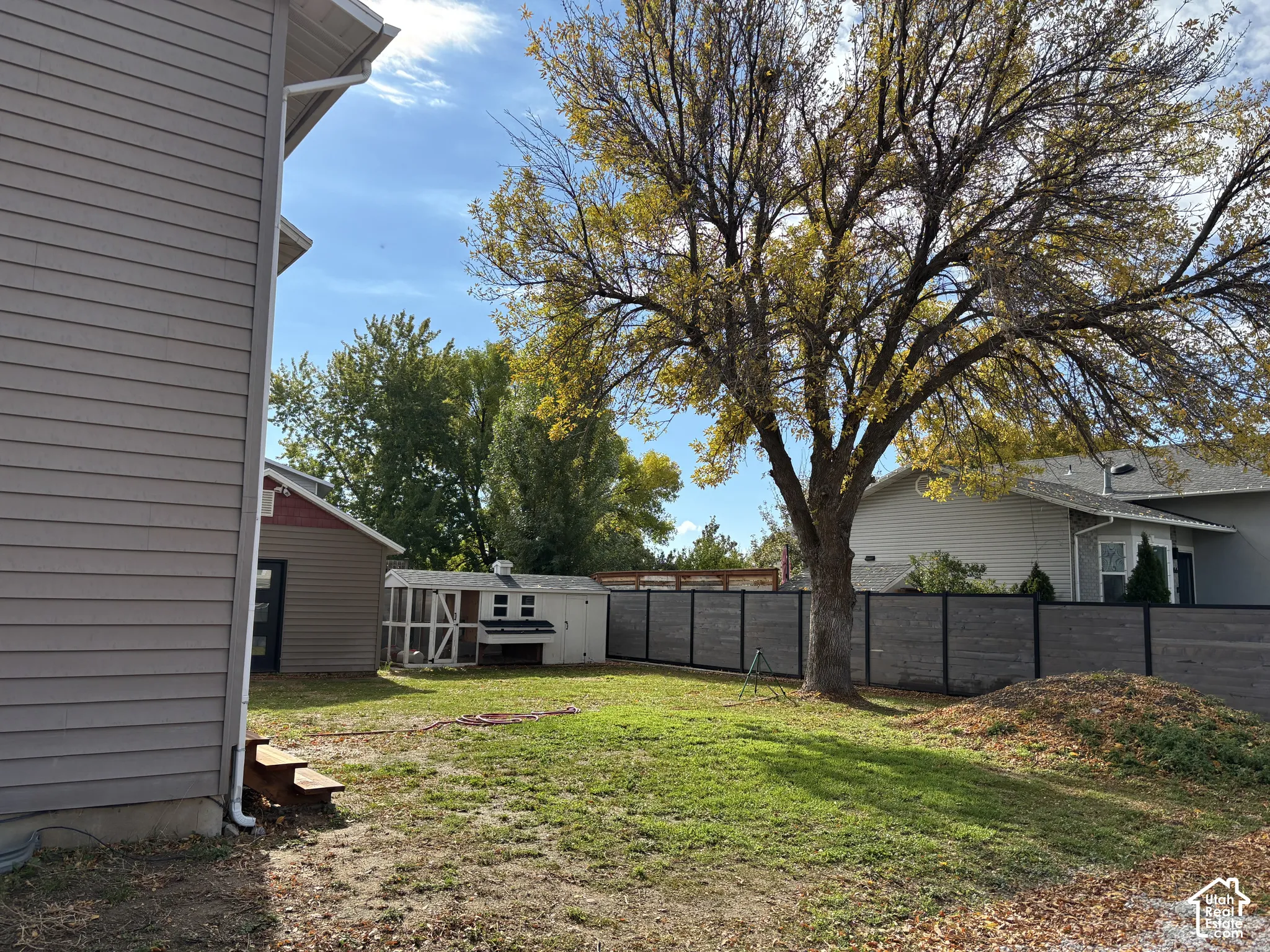 Backyard featuring horizontal panel fencing, mature trees, and a detached outbuilding