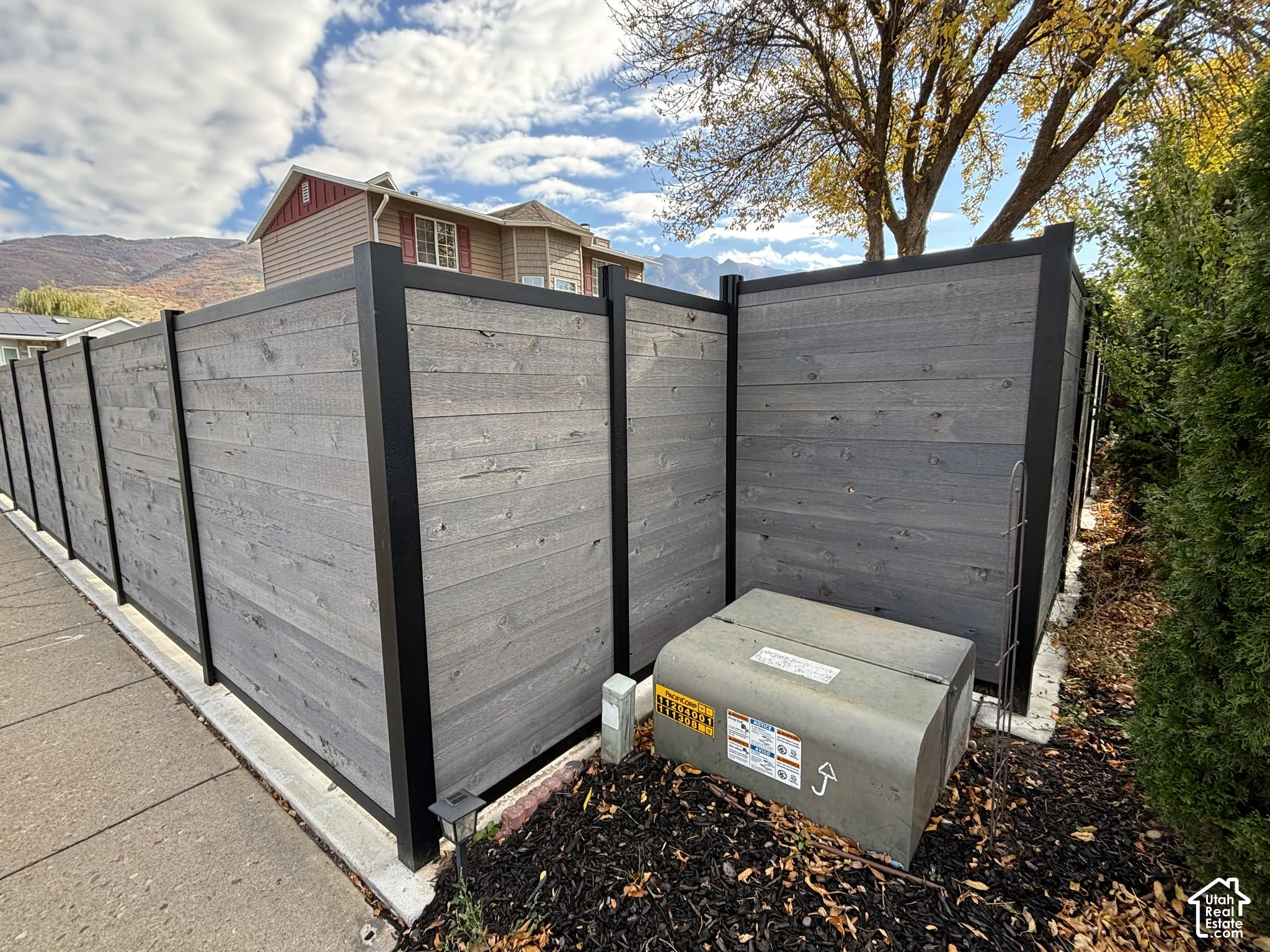 Full-height privacy fencing featuring horizontal wood-finish planks and a black metal frame, grounded by a concrete base and mulched landscaping beds