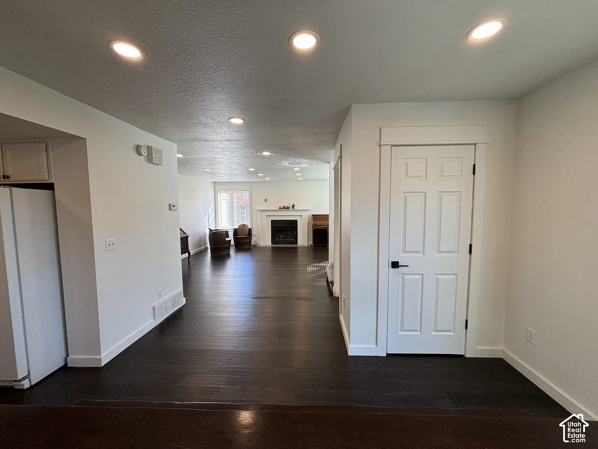 Dark wood-finish flooring, recessed lighting, fireplace with a mantel, and paneled interior door with matte black hardware
