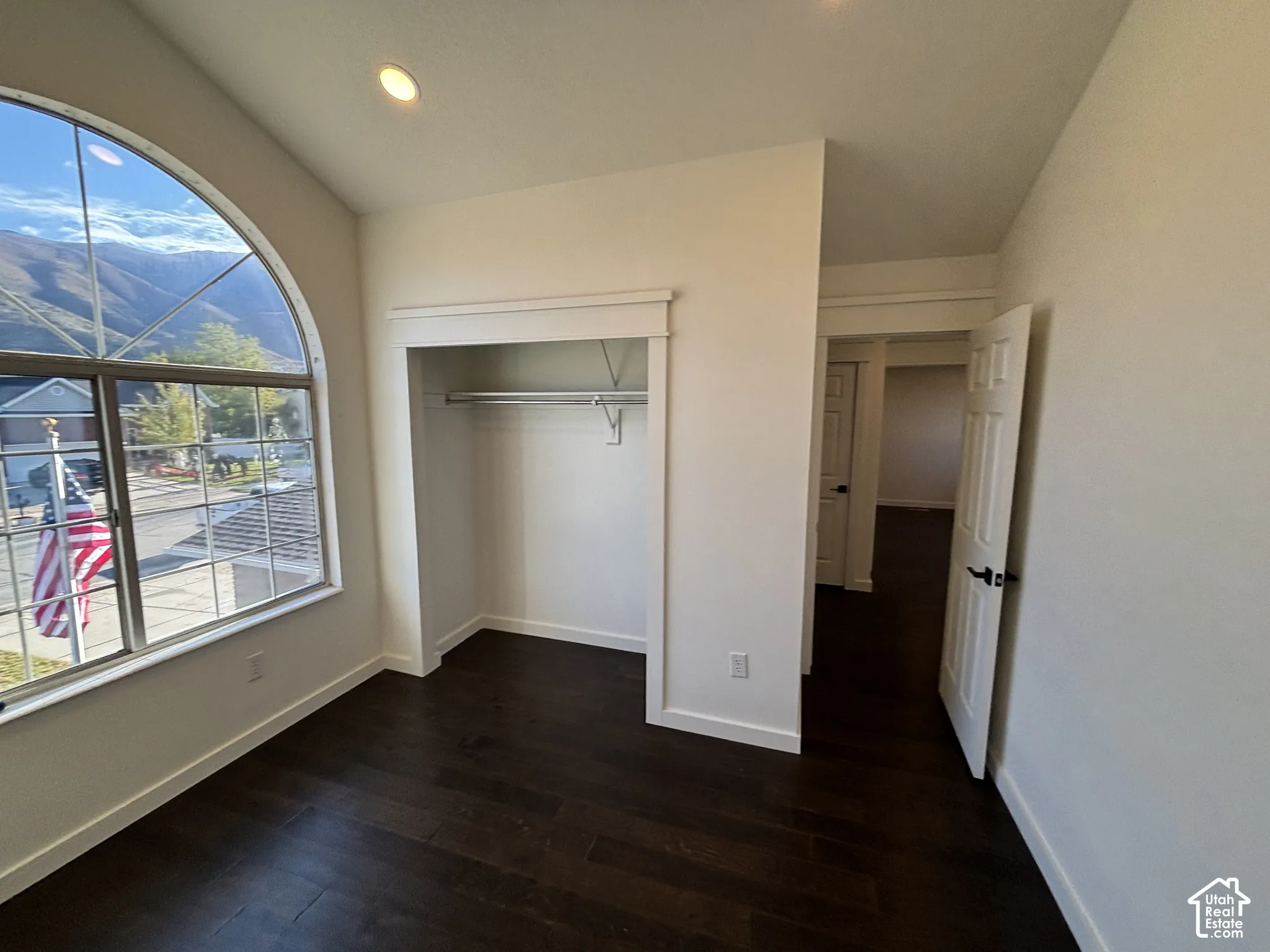 Arched window with mountain scenery, dark wood-finish flooring, recessed ceiling lighting, and built-in closet with overhead trim detail