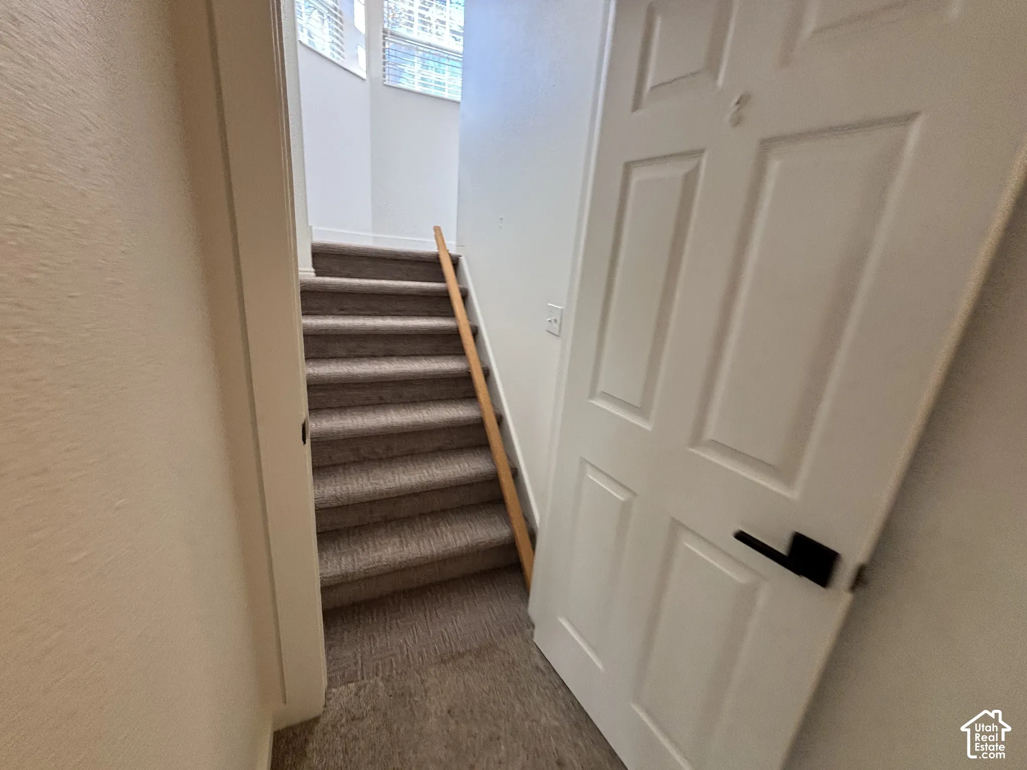 Staircase featuring wall-to-wall carpeted treads, a natural wood handrail, and white interior doors with matte black hardware