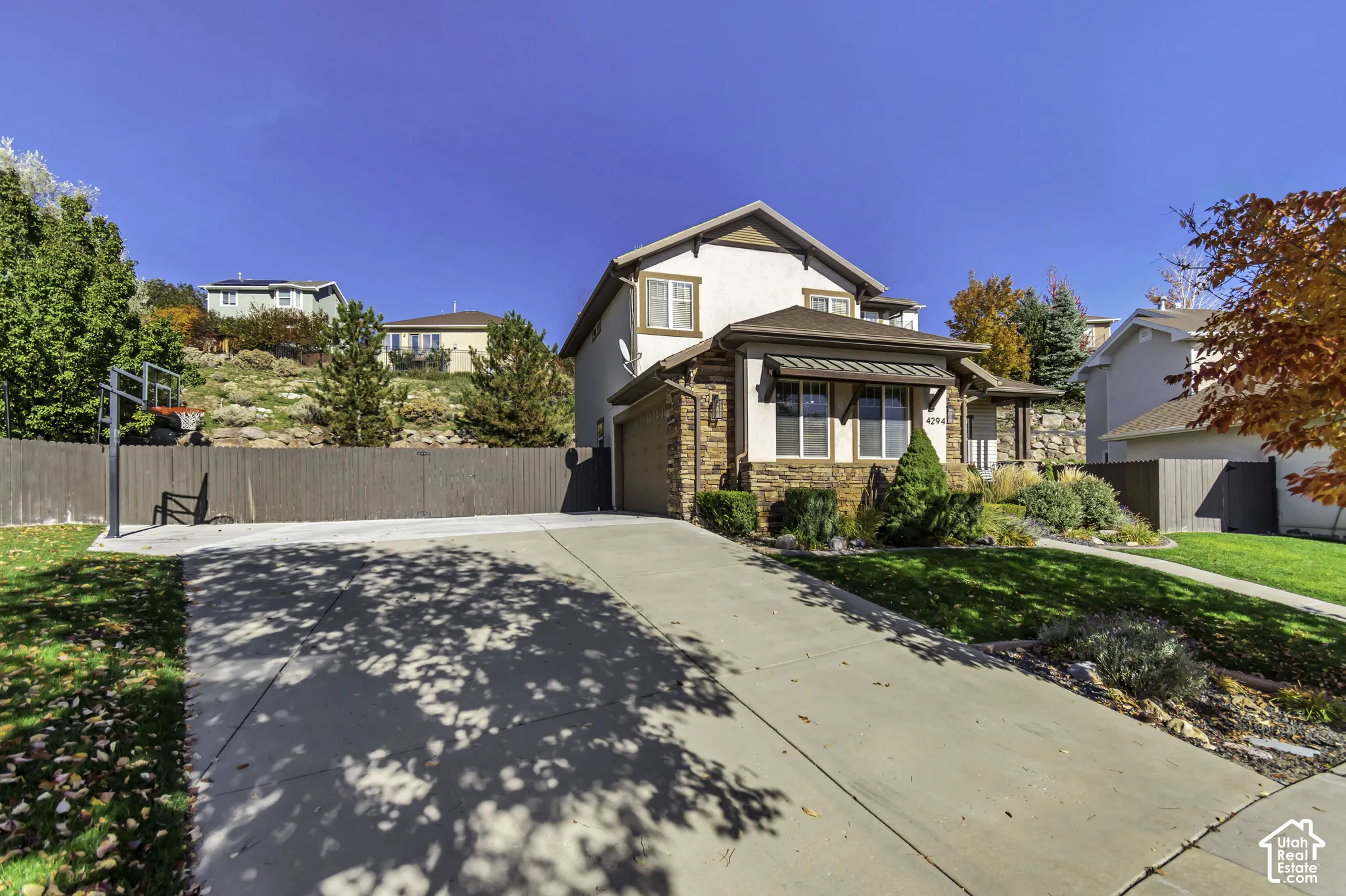 Two-story residence featuring a stucco and stone exterior, concrete driveway, attached garage, metal awning over front windows, and wood-style perimeter fencing