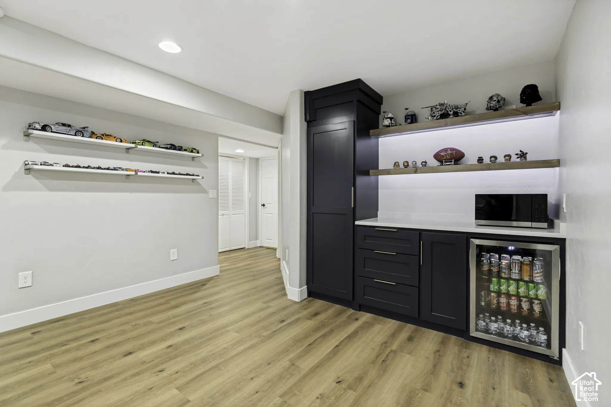 Custom kitchenette featuring dark-finish cabinetry, quartz countertops, integrated under-counter beverage refrigerator, recessed lighting, and wood-finish flooring
