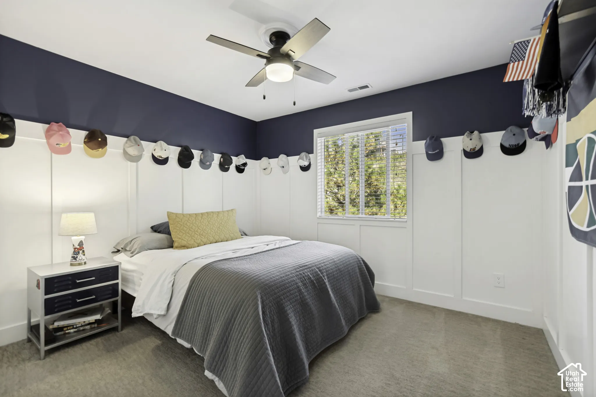 Board-and-batten wainscoting, neutral carpeting, multi-blade ceiling fan with integrated lighting, and horizontal window blinds