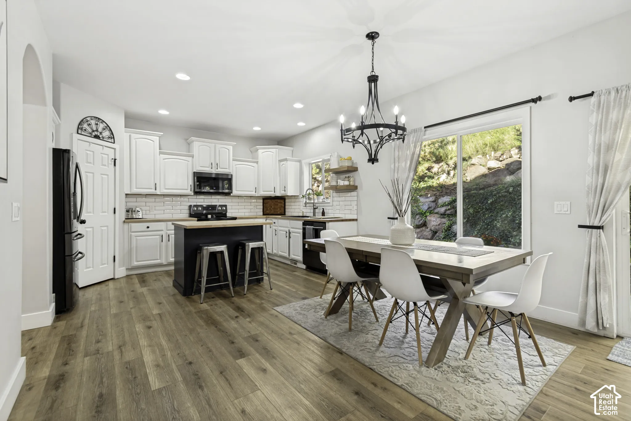 Kitchen featuring white shaker-style cabinetry, wood-finish flooring, a central island with a wood countertop, a subway tile backsplash, and a multi-arm chandelier